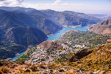 Aerial view of the white washed village of guejar sierra on the foot of the Sierra Nevada next to the blue guerja Embalse lake.