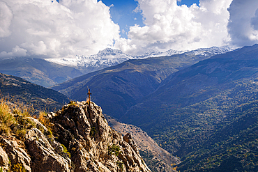 Snow-capped Sierra Nevada mountains rising above forested valleys and a cross on a rock, viewed from the Mountains in Guerja Sierra, Granada province, Spain.
