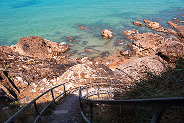 A charming stone staircase descends toward the rocky shoreline and crystal-clear waters of Brittany, France