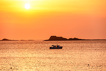 Orange hazy sunset above the Northern Sea with some channel island seen as black silhouettes. France