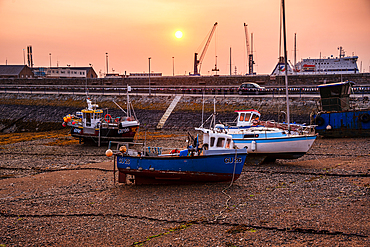 Fishing boats resting on the seabed at low tide in St Peter Port harbor, Guernsey, Channel Islands, at a hazy sunrise