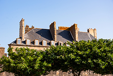 historic stone houses with chimneys behind green trees in Saint-Malo Brittany France
