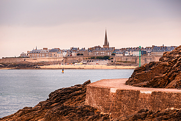 Panoramic coastal view of Saint-Malo walled city with spire and stone ramparts Brittany France. Coastal walkway of Dinard in the foreground