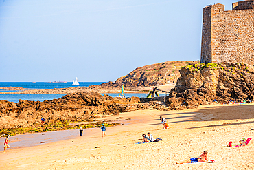 Tourists on sandy beach by Saint-Malo city walls and rocky coast Brittany France