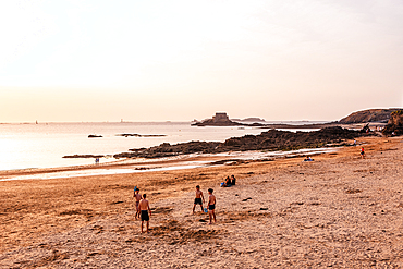 Tourists walking on sandy beach near Fort National and Saint Malo ramparts at sunset Brittany France. Relaxed evening scene of visitors enjoying the beach at Saint-Malo