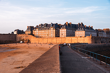 Golden hour view of the walled city of Saint-Malo with its medieval ramparts and granite houses reflecting warm sunlight over the sandy beach