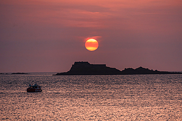 Golden-red evening sky over the English Channel with Fort National silhouetted in the distance and small boats floating offshore.