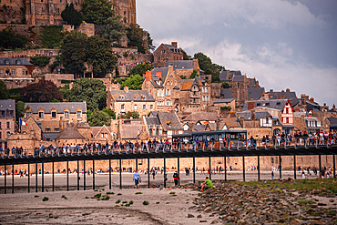 A detailed view of the lower village and ramparts of Mont Saint-Michel and the bridge full of tourist entering the old town, Normandy, during low tide.