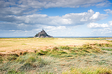 A sweeping landscape view of Mont Saint-Michel, Normandy, France, rising dramatically from the vast tidal flats that surround the island.