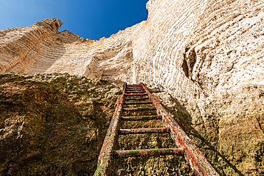 Rustic metal ladder steps descend toward the towering limestone walls of Étretat’s cliffs on the Normandy coast.