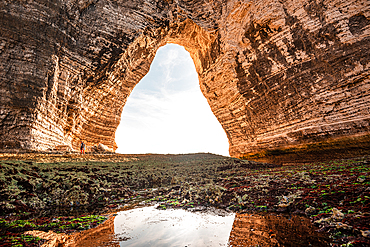 Perspective from inside a sea cave at Étretat, Normandy, looking out toward the sky through a natural chalk arch.