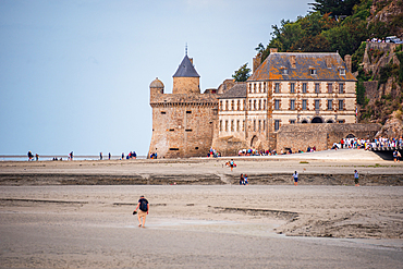 People walking along the sandy beach near Mont Saint-Michel, Normandy, France.