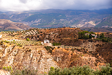 Andalusian countryside near Durcal with isolated farmhouses, olive groves, and rugged badlands leading to distant mountains.