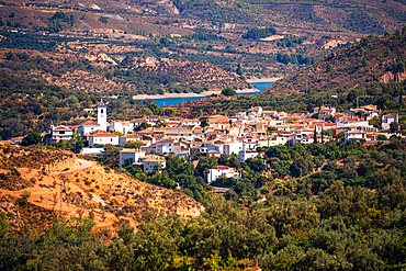 A panoramic view of Restábal, Granada, with whitewashed houses surrounded by olive groves and the embalse de beznar in the background