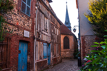 Narrow cobbled street with medieval half-timbered houses in Honfleur’s historic district, with church spire in the background.