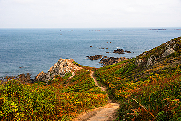Coastal walking path leading down to rocky cliffs and the sea at Pleinmont Point, Guernsey, Channel Islands, UK. Rugged coastline and scenic ocean view under soft afternoon light.