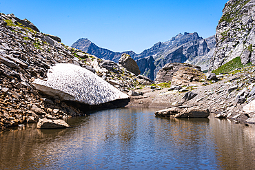 Remains of a snow field in the Alps melting into a lake on an alpine mountain pass, the Alps, Piemonte (Piedmont) Northern Italy, Europe