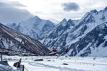 Helicopter landing on a snowy field in front of high altitude mountain landscape with Gangchempo summit, Langtang Valley Trek, Himalayas, Nepal, Asia