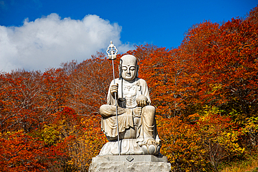 Big shizo statue in front of fire red autumnal leaves at beautiful Japanese temple surrounded by autumn colors, Osorezan Bodaiji Temple, Mutsu, Aomori prefecture, Honshu, Japan, Asia