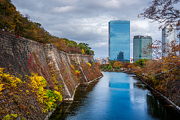 View along the inner Osaka Castle moat with autumnal trees and Crystal tower and CBD in the background, Osaka, Honshu, Japan, Asia