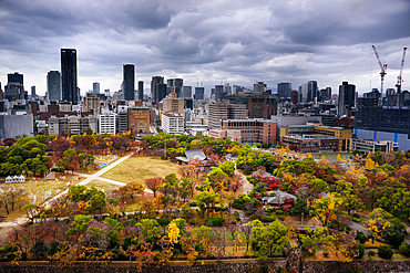 Looking over the castle park onto the city skyline with dramatic sky in autumn, Osaka, Honshu, Japan, Asia