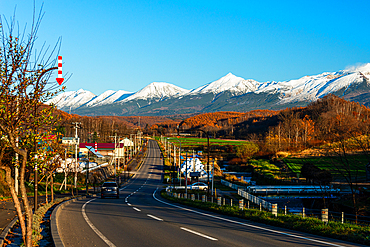 Alpine panorama of rural area with highway leading to the snowy Tokachi mountain range in Hokkaid , Japan, Asia