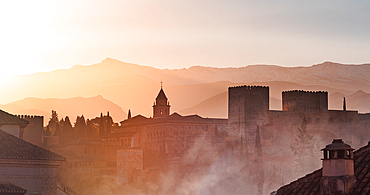 Atmospheric sunrise over the Alhambra, capturing the historic architecture silhouetted against the warm, golden hues of the Sierra Nevada mountains in the background. Mist and ancient fortress, adding a mystical iconic view of Granada, Spain.