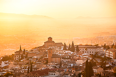 Beautiful atmospheric hazy sunset above the historic Albaicin, Granada, Andalucia, Spain. Warm orange light over the valley. View from San Miguel alto over the Albaicin alto and iglesia de San Cristóbal.