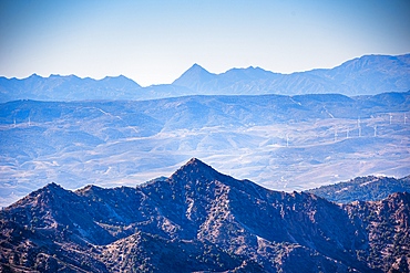 Distant view of layered mountain ranges with a prominent peak, overlooking arid valleys under a clear blue sky, Triangle shaped mountains of Sierra Nevada and Sierras de Tejeda, Almijara y Alhama align