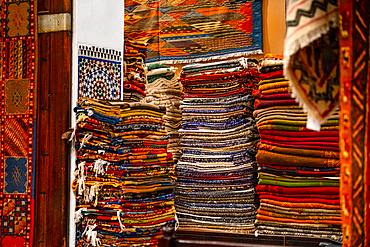 Stacks of vibrant handwoven Moroccan rugs and carpets displayed in a traditional shop in Fes, showcasing intricate patterns and craftsmanship.