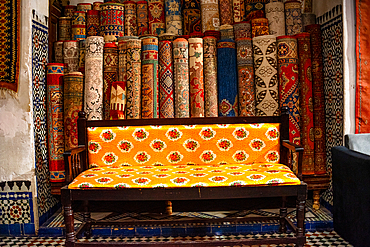 Stacks of vibrant handwoven Moroccan rugs and carpets displayed in a traditional shop in Fes, showcasing intricate patterns and craftsmanship