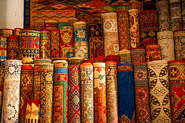 Stacks of vibrant handwoven Moroccan rugs and carpets displayed in a traditional shop in Fes, showcasing intricate patterns and craftsmanship