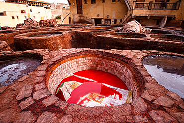 Vibrant red dye in a traditional leather tannery pit in Fes, Morocco, surrounded by historic stone basins and rustic architecture