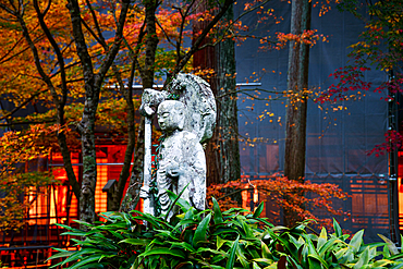 A Jizo statue adorned with vines, standing amidst vibrant greenery and autumn trees in the peaceful grounds of Sanzen-in Temple.