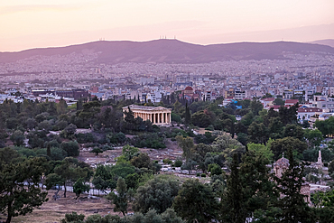 Athens, Greece – Sunset view of the Héphaïstéion (Temple of Hephaestus) standing among trees in the Ancient Agora (Αρχαία Αγορά), with Athens’ urban landscape stretching beyond.