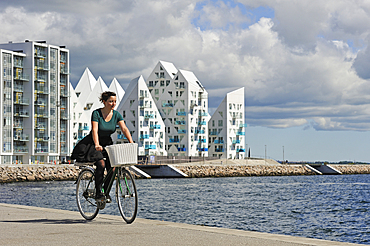 young woman cycling with, in the background, The Iceberg apartment building in the new quarter Aarhus Ø constructed by the expansion of the harbour area, Aarhus, Jutland Peninsula, Denmark, Northern Europe