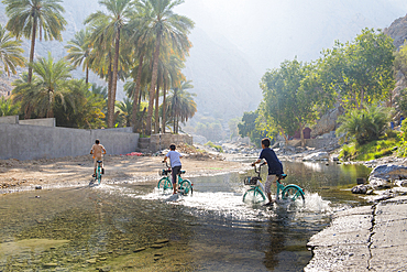 Kids on bicycles crossing the river near the Al Thowarah hot spring (Nakhal spring), Sultanate of Oman, Arabian Peninsula