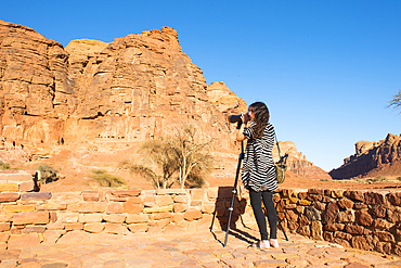 People observing, with binoculars, the tombs cut into the red rock cliffs at Archaeological site of Dadan, the ancient capital of the Dadan And Lihyan kingdoms more than 2000 years ago. AlUla, Medina Province, Saudi Arabia, Middle East