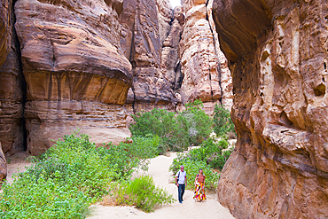 Two people walking at the bottom of a canyon with sandstone walls in the Sharaan Nature Reserve, AlUla, Medina Province, Saudi Arabia, Middle East