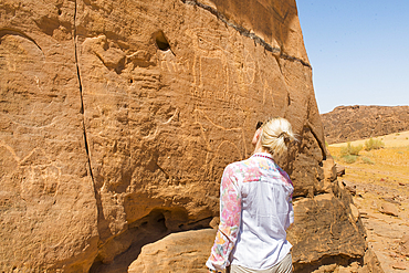 Woman admiring ancient symbols and rock carvings on a sandstone rock cliff in the Sharaan Nature Reserve, AlUla, Medina Province, Saudi Arabia, Middle East