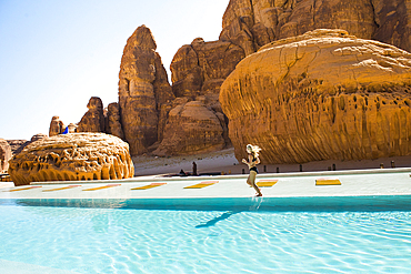 Woman running on the edge of the swimming pool of Our Habitas AlUla, a sustainable desert luxury resort nestled within an ancient oasis in the desert canyons of the Ashar Valley, Medina Province, Saudi Arabia, Middle East