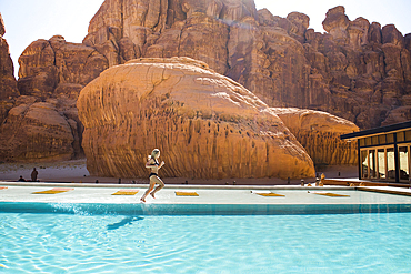 Woman running on the edge of the swimming pool of Our Habitas AlUla, a sustainable desert luxury resort nestled within an ancient oasis in the desert canyons of the Ashar Valley, Medina Province, Saudi Arabia, Middle East