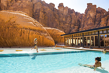 Woman running on the edge of the swimming pool of Our Habitas AlUla, a sustainable desert luxury resort nestled within an ancient oasis in the desert canyons of the Ashar Valley, Medina Province, Saudi Arabia, Middle East