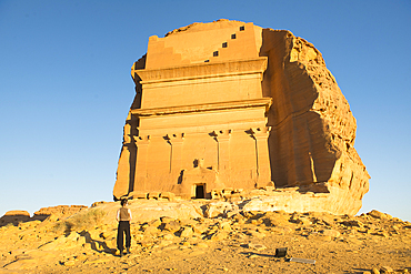 Standing up woman admiring the Tomb of Lihyan son of Kuza (Qasr AlFarid), carved into its own separate sandstone outcrop within the UNESCO World Heritage Site of Hegra, AlUla, Medina Province, Saudi Arabia, Middle East