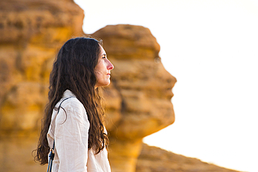 Woman posing in front of the 'Face Rock', a sandstone rock formation shaped like the human head profil, within the UNESCO World Heritage Site of Hegra, AlUla, Medina Province, Saudi Arabia, Middle East