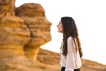 Woman posing in front of the 'Face Rock', a sandstone rock formation shaped like the human head profil, within the UNESCO World Heritage Site of Hegra, AlUla, Medina Province, Saudi Arabia, Middle East