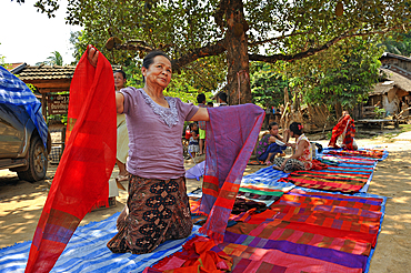 Villager showing clothes and local crafts for sale to tourists passing through Ban Baw, a traditional Lao Loum village by the Mekong River, between Luang Prabang and Pakbeng, Laos, Southeast Asia