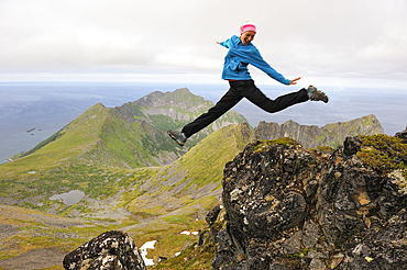 Young woman jumping at the top of the Husfjellet mountain, Senja island, County of Troms, Norway, Northern Europe