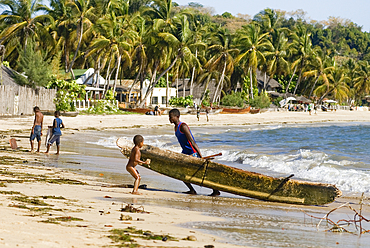 Fisherman hauling up his outrigger canoe on the beach of Ambatoloaka, Nosy Be island,Republic of Madagascar,Indian Ocean