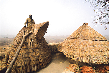 Tammari (also known as Batammariba, Tamberma, Somba, Otamari) man coming out of a granary on the roof his fortified house, known as Tata Somba ('Somba house'), Atakora department, Benin, Gulf of Guinea, West Africa